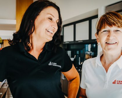 Two women in black shirts standing in a kitchen.