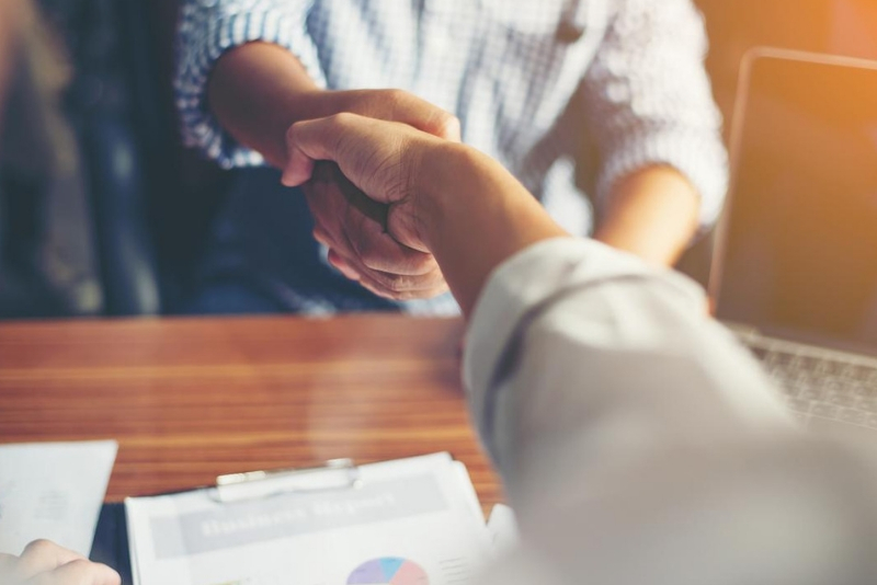 Two people sitting at a desk handshake.