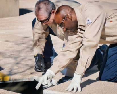 Two men working on a drain in a parking lot.