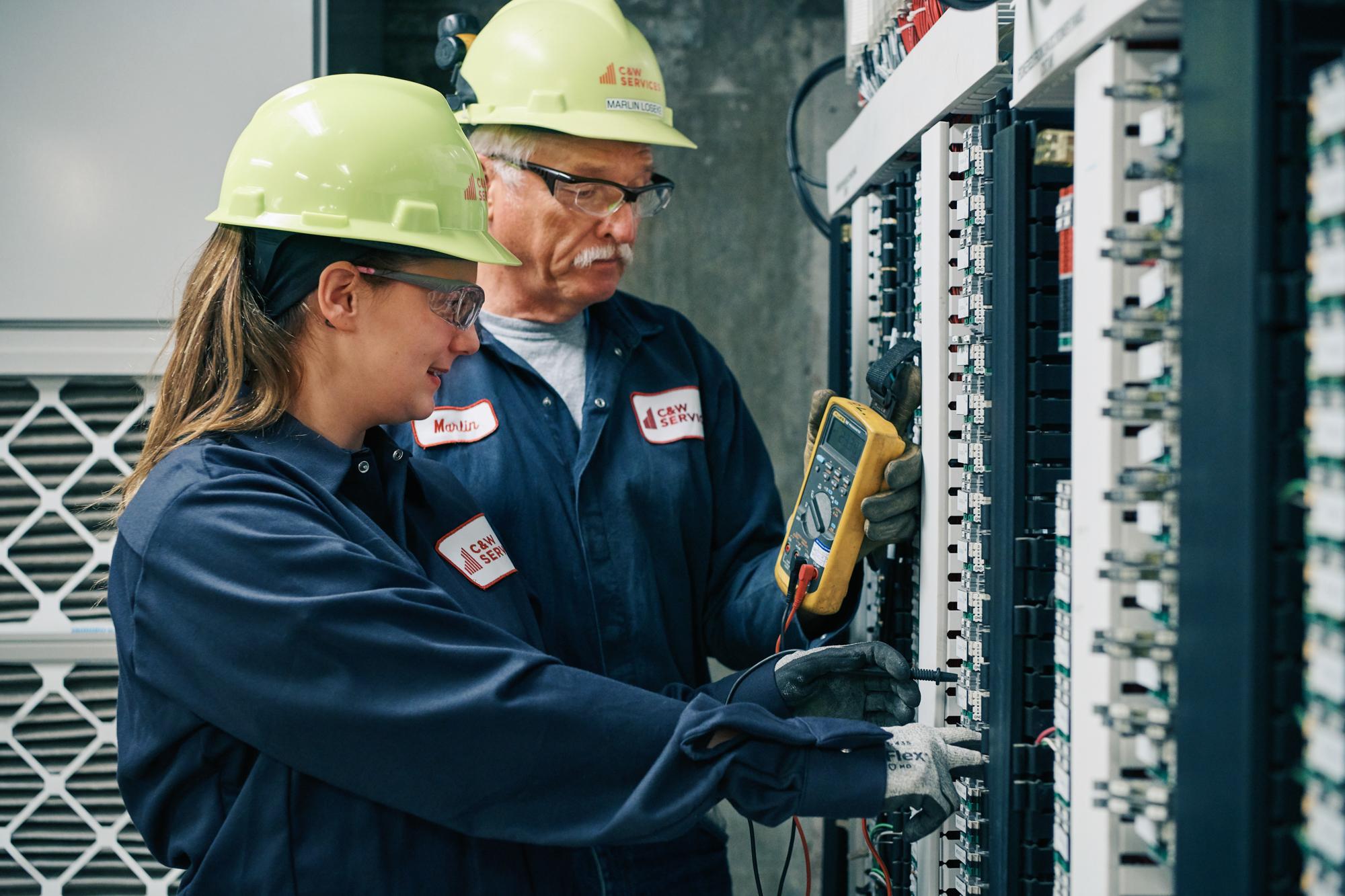 Two electricians working on an electrical panel.