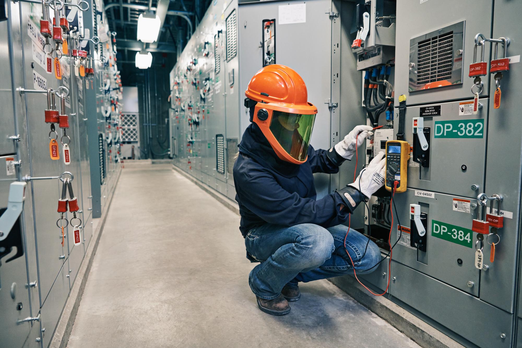 A worker wearing an orange safety helmet is working on an electrical panel.