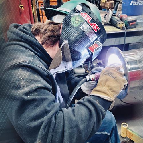 A man welding a metal piece in a workshop.