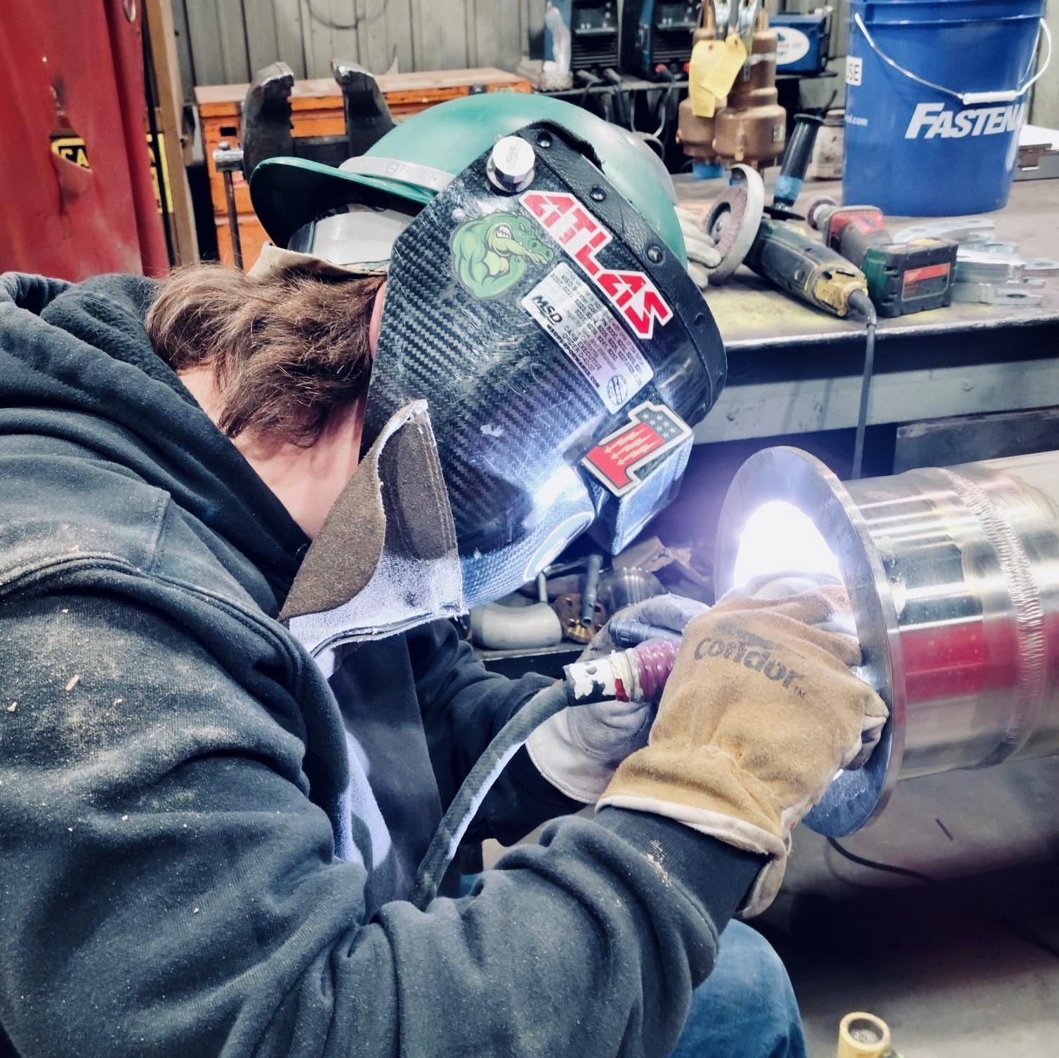A man welding a metal pipe in a workshop.
