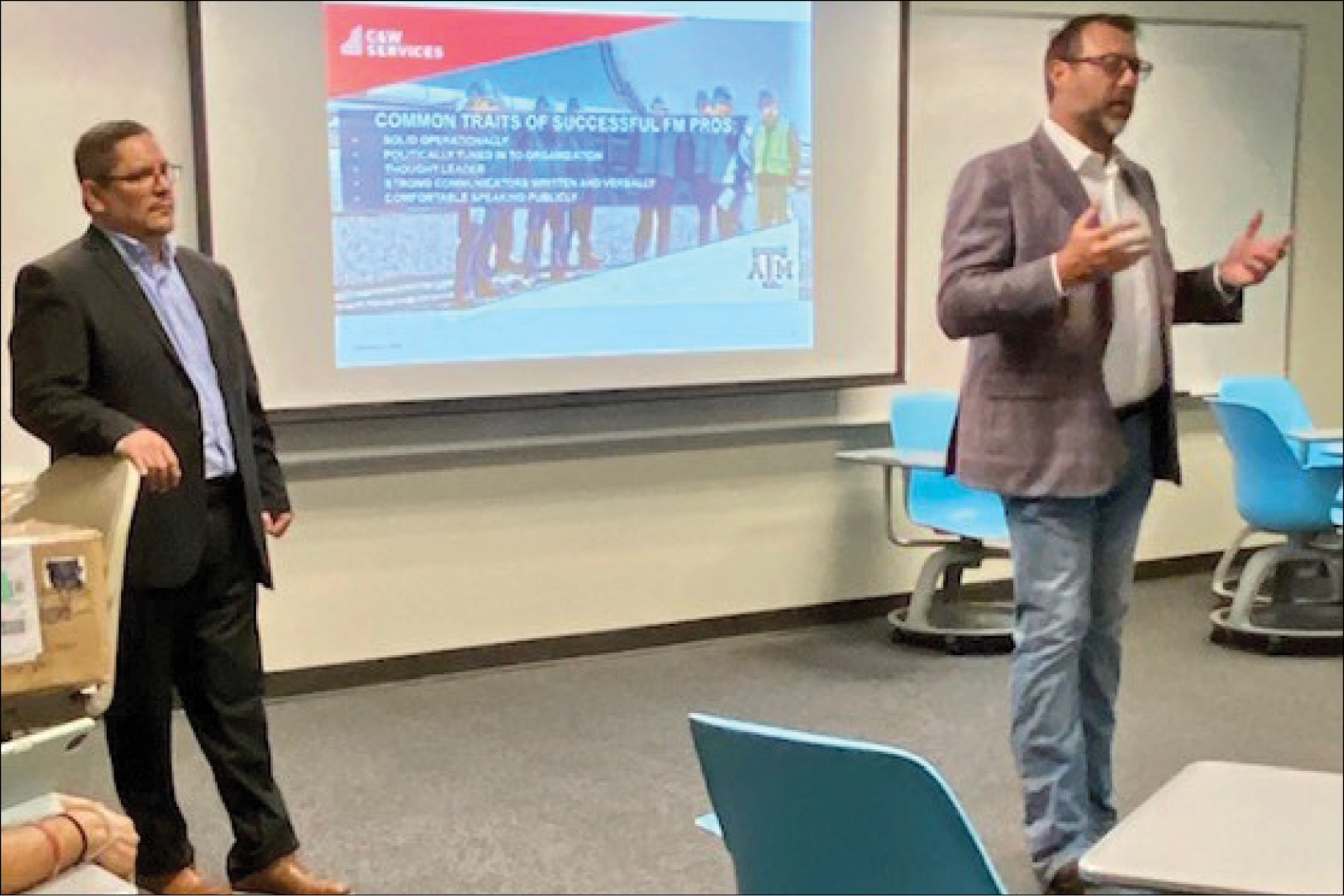 Two men standing in front of a projector in a classroom.