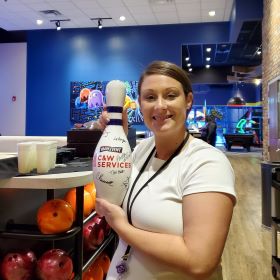 A woman holding a bowling pin in a bowling alley.