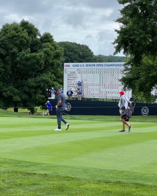 Bill Ayres and his caddy approaching the tee with scoreboard in the background