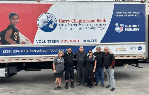 A group of people standing in front of a truck that says harry chapman food bank.