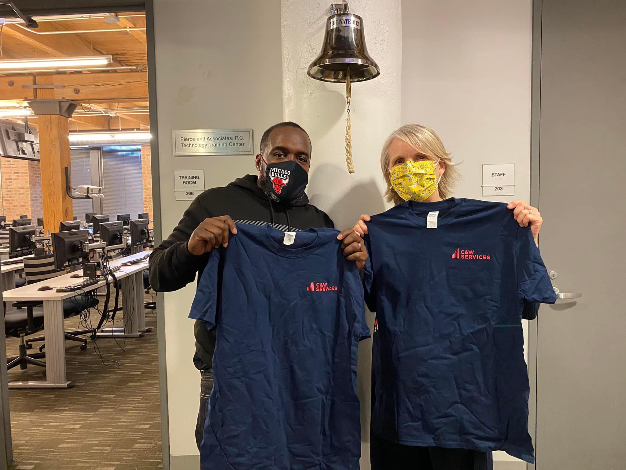 Two people wearing masks in an office holding t - shirts.