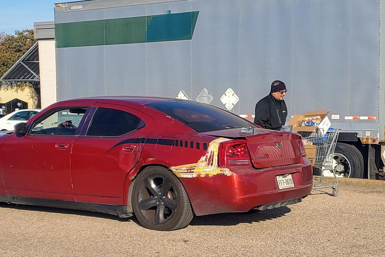 A red dodge charger parked in front of a truck.