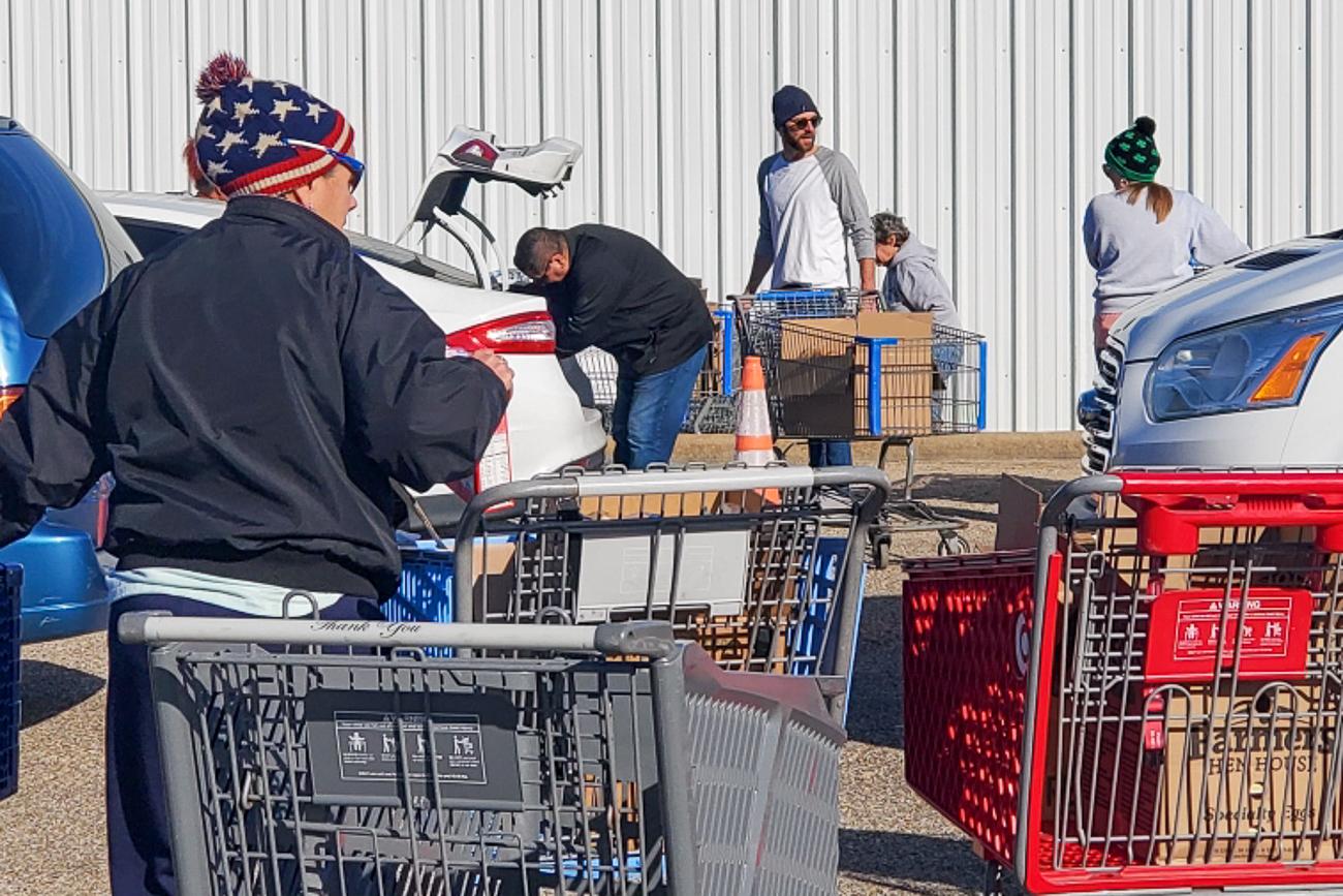A group of people with shopping carts in a parking lot.