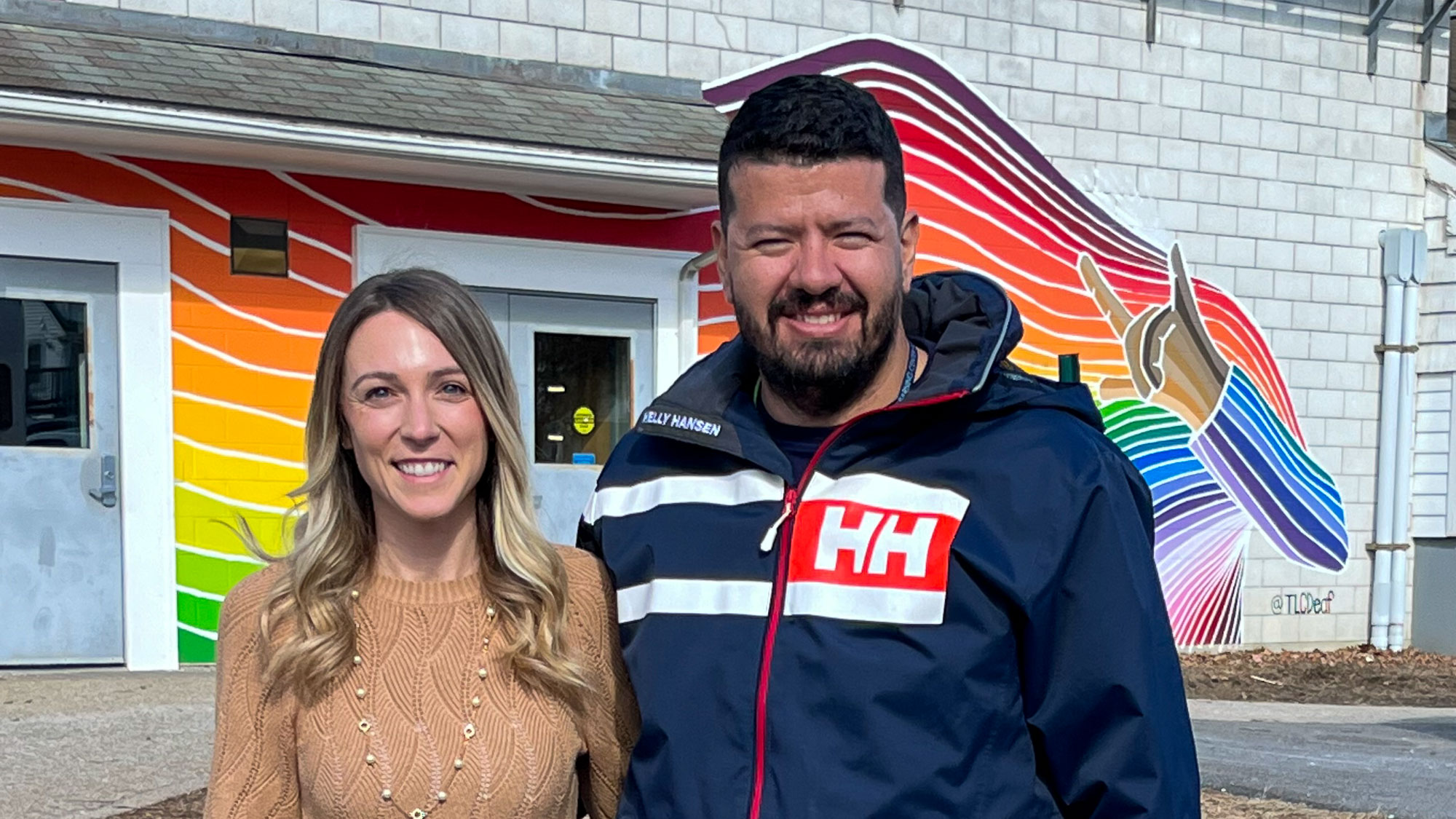 Woman and man standing in front of a mural painted on the side of a school building.