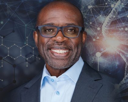 A man in glasses is smiling in front of a dna background.