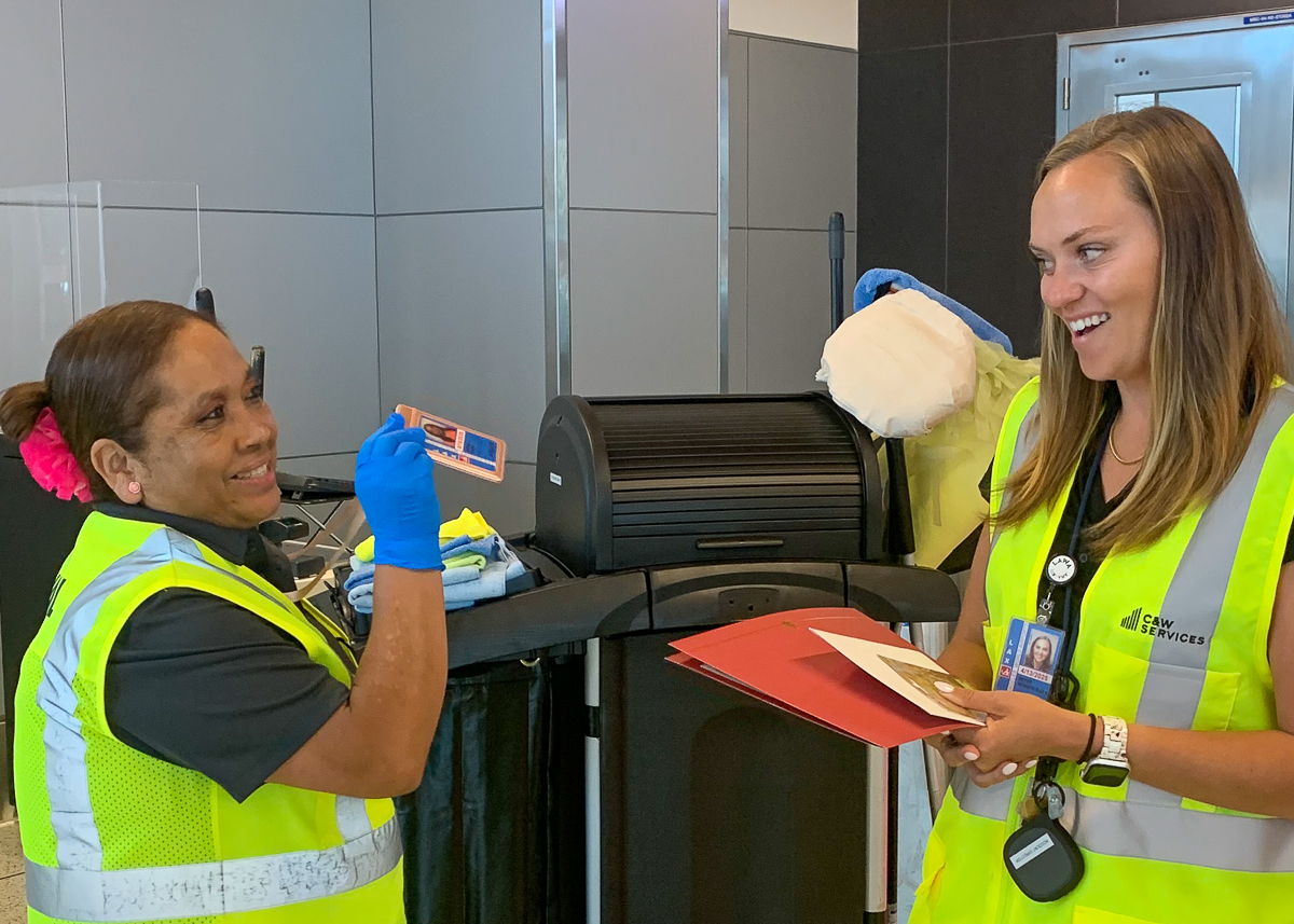 Two smiling women wearing safety vests. One woman gives another a certificate of appreciation and a gift card.
