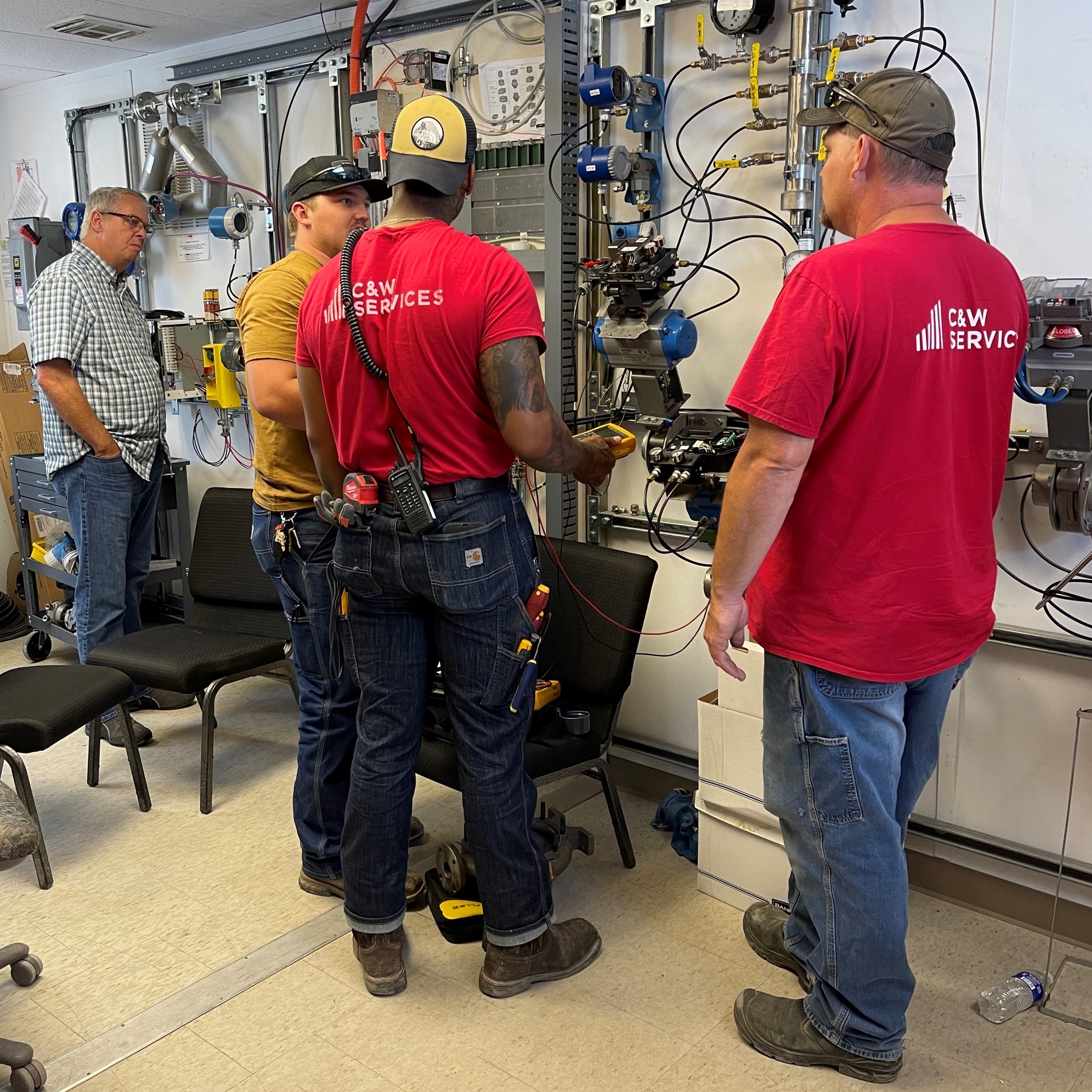 A group of men in C&W Services shirt being shown how to use maintenance equipment
