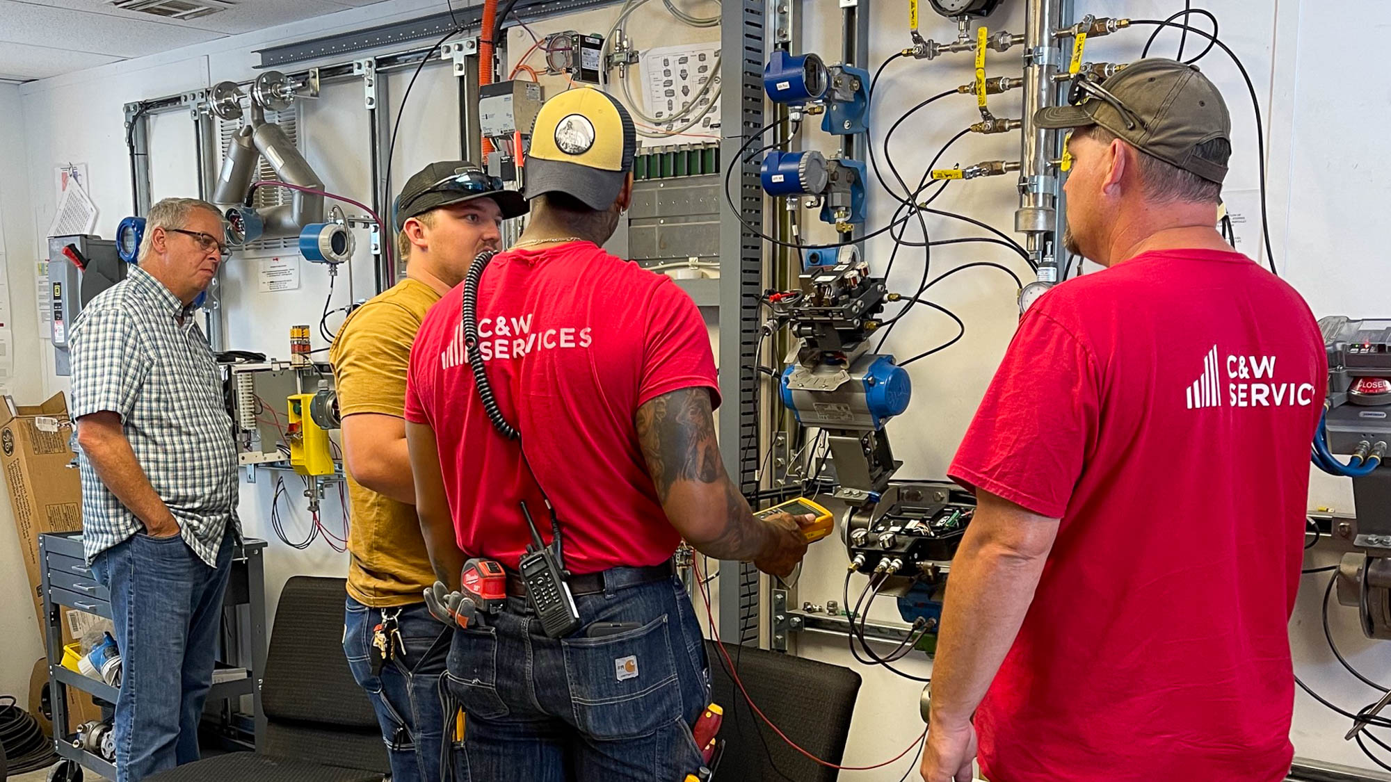 A group of men in C&W Services shirt being shown how to use maintenance equipment