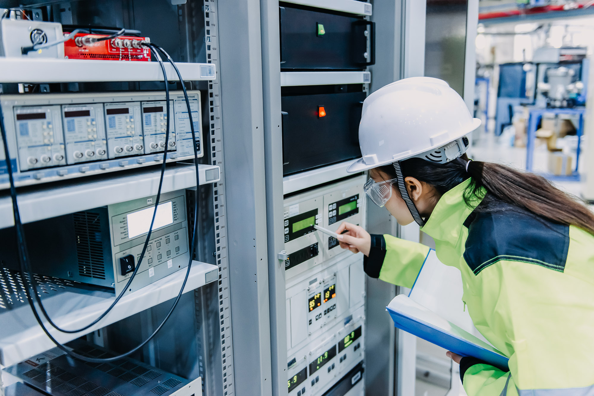 A woman in a hard hat is looking at equipment in a factory.