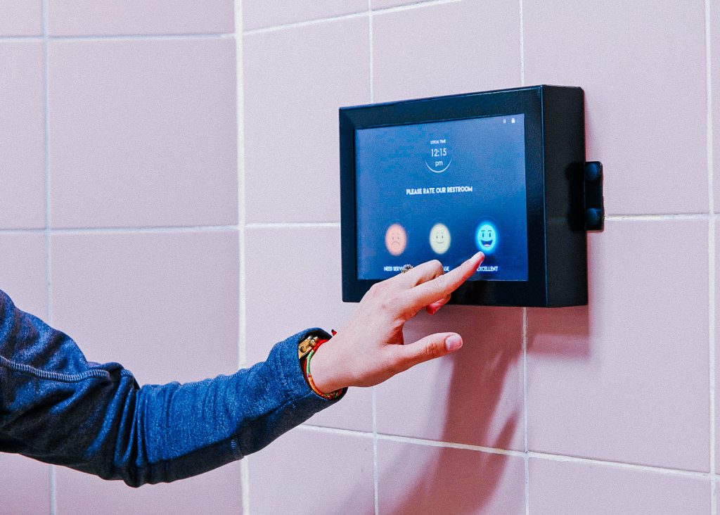 A person using a touchscreen to rate the cleanliness of a restroom.