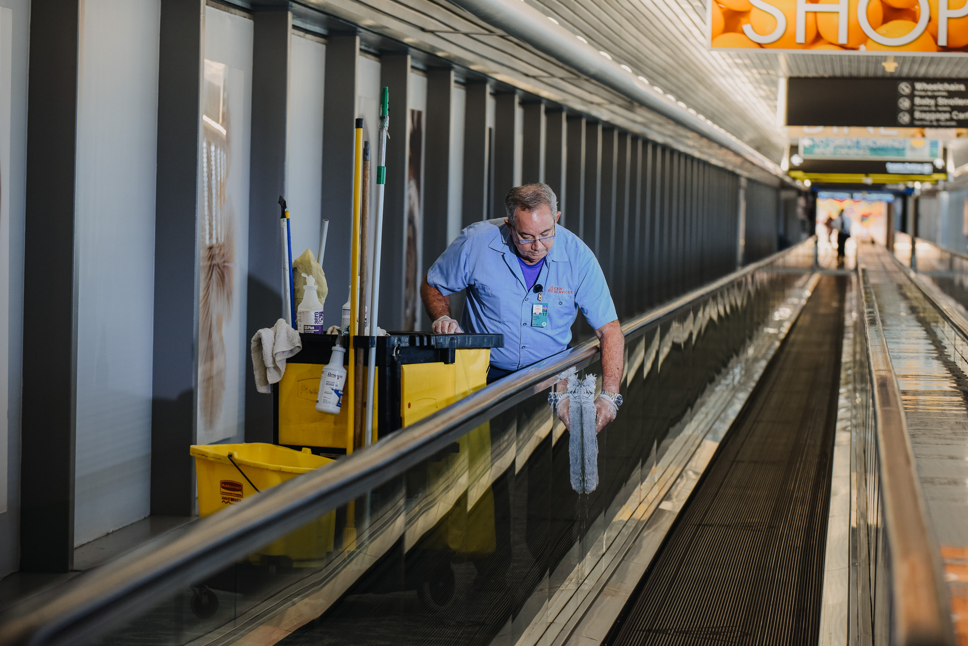 A man cleaning a moving walkway at an airport.