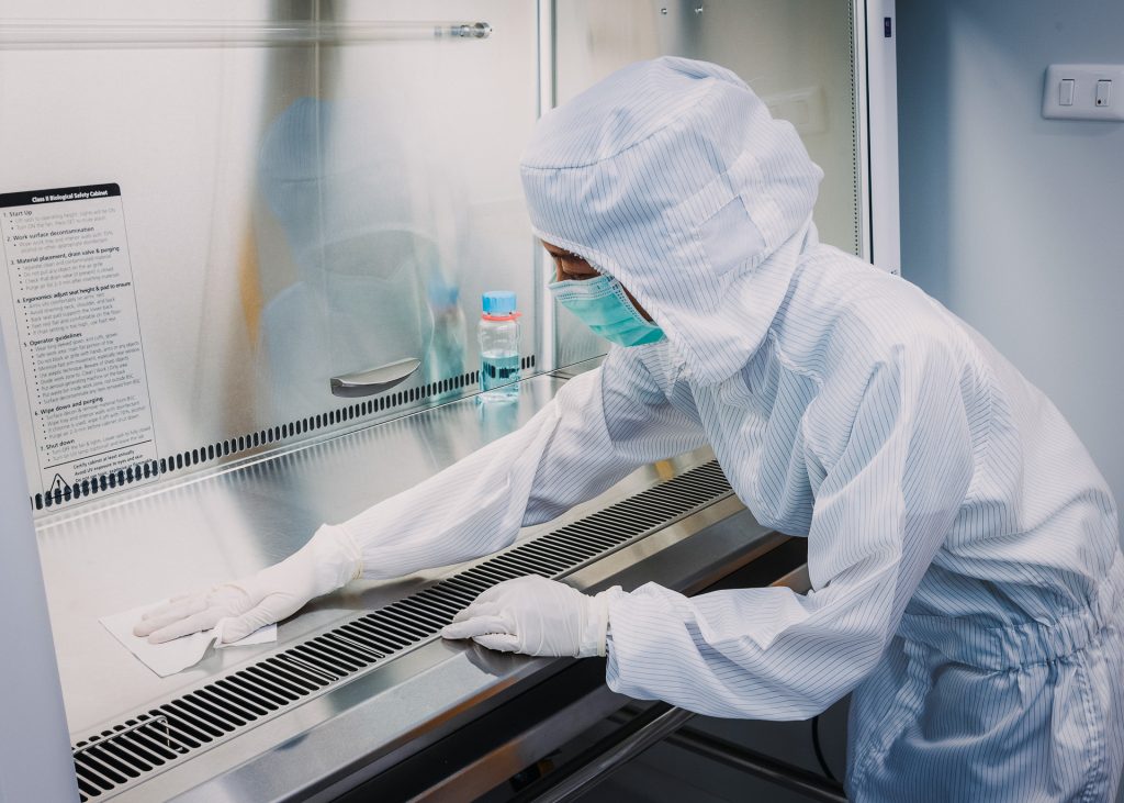 A person in a white lab coat sterilizing a counter.