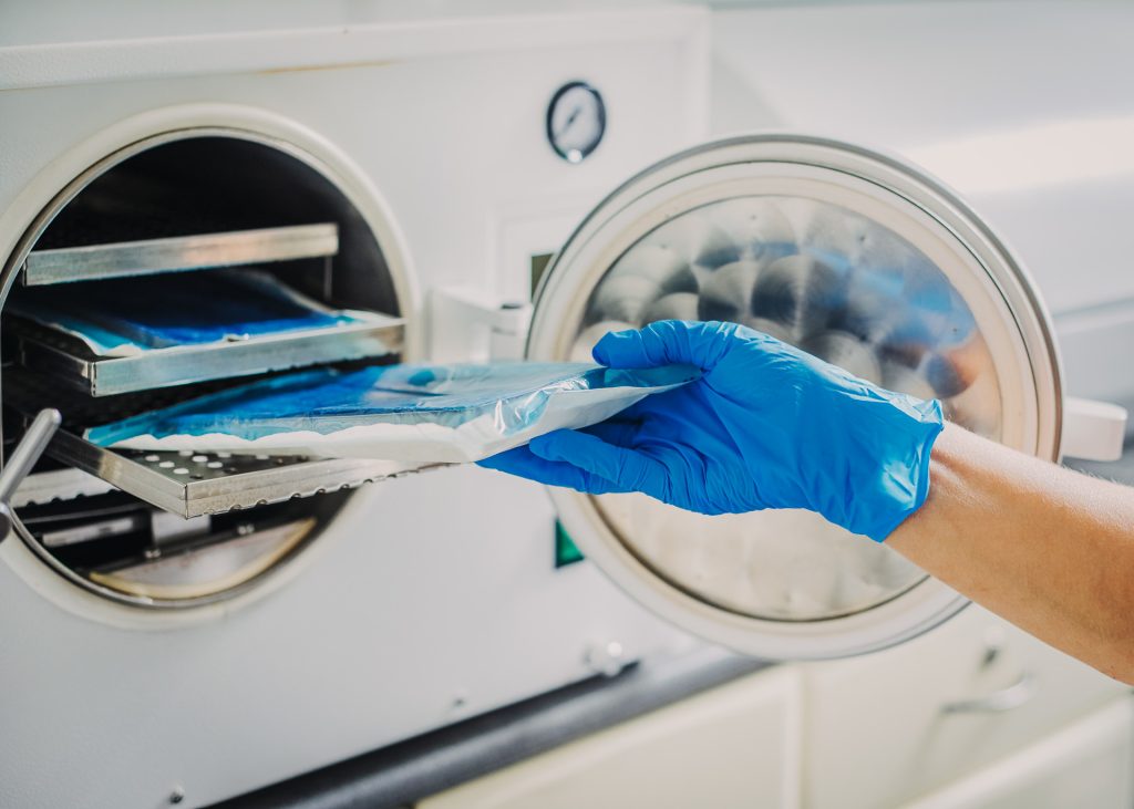 A woman in blue gloves putting a tray into a sterilization machine