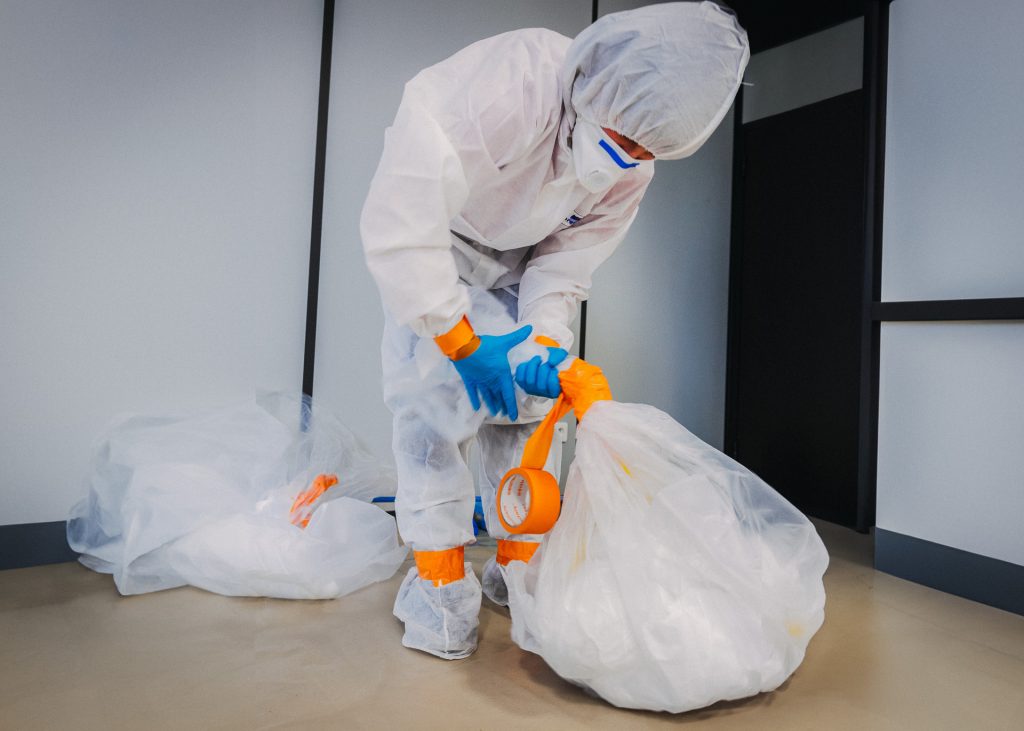 A person in a protective suit securing waste in a garbage bag.