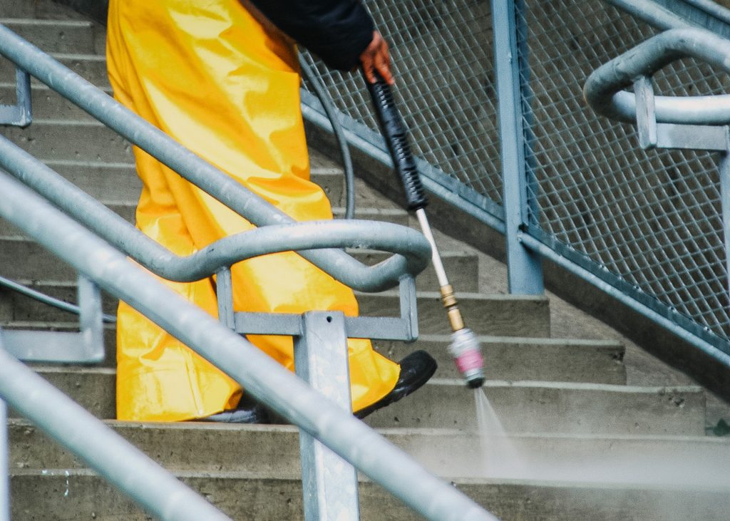 A man in a yellow raincoat cleaning stairs with a pressure washer.