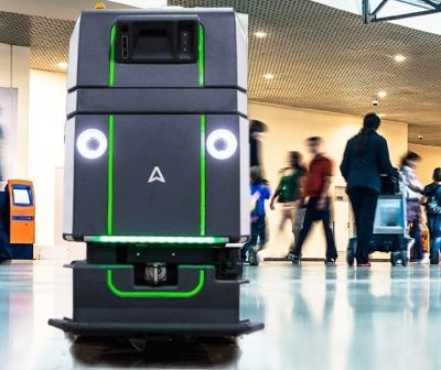 A robot walking through an airport with people around it.