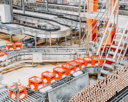 A conveyor belt in a factory with orange bottles on it.