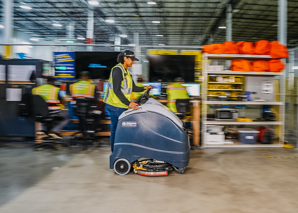 A woman using a robot to clean a floor in a warehouse.