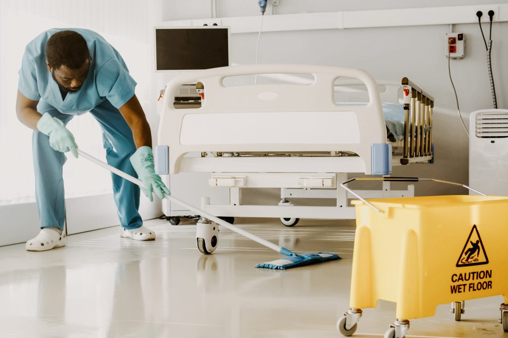 A man cleaning a hospital room with mop and bucket.