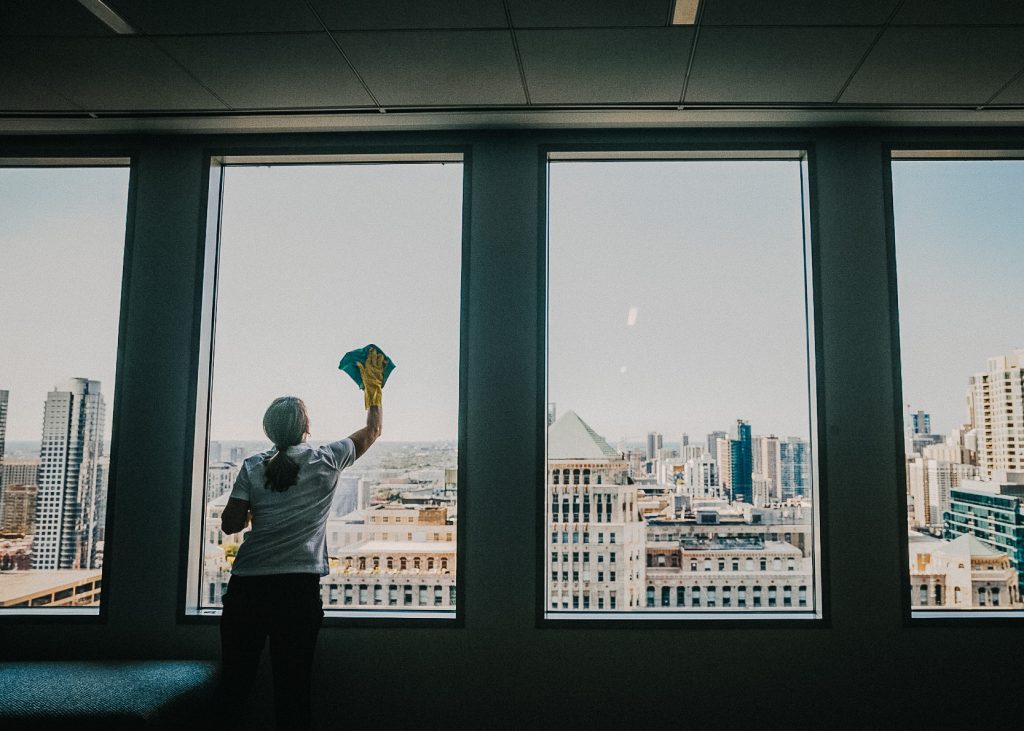 A woman cleaning a window in an office with a view of the city.