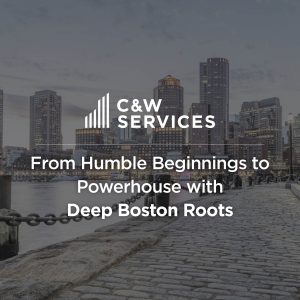 C&W Services text overlay on an image of a Boston waterfront with cobblestones, buildings, and a chain railing. The text reads: "From Humble Beginnings to Powerhouse with Deep Boston Roots".