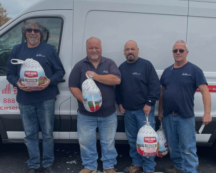 Four men in blue shirts and jeans hold turkeys in front of a white service van in a parking lot.