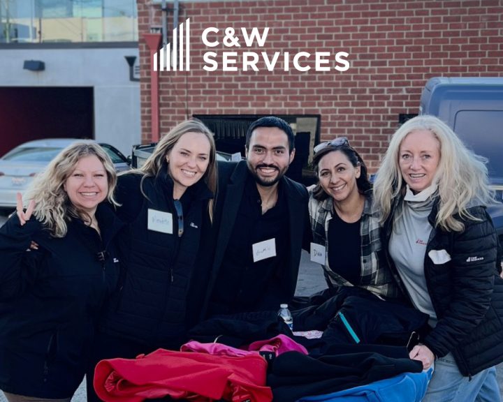 Five people smiling together near a table with colorful clothes under the C&W Services sign.