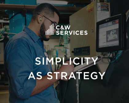 A man in work attire uses a tablet and reads notes in an industrial setting; a C&W Services logo and the text 