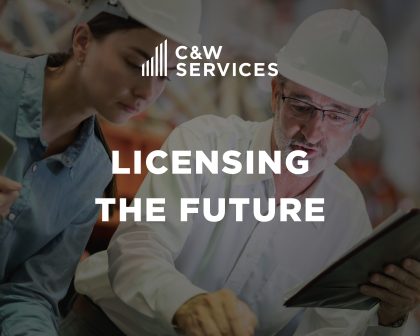 Two people wearing hard hats review plans or documents in an industrial setting. Text overlay reads 