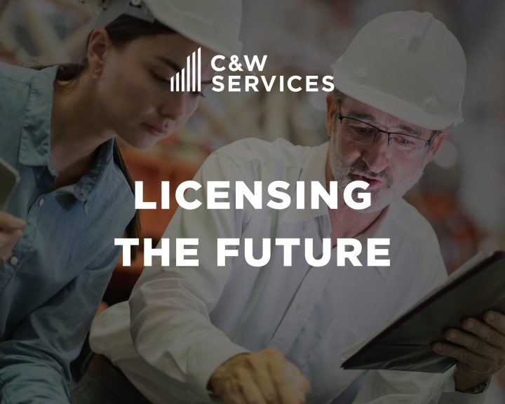 Two people wearing hard hats review plans or documents in an industrial setting. Text overlay reads 